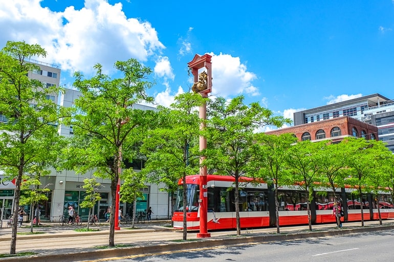 long red streetcar with green trees in front in toronto chinatown.