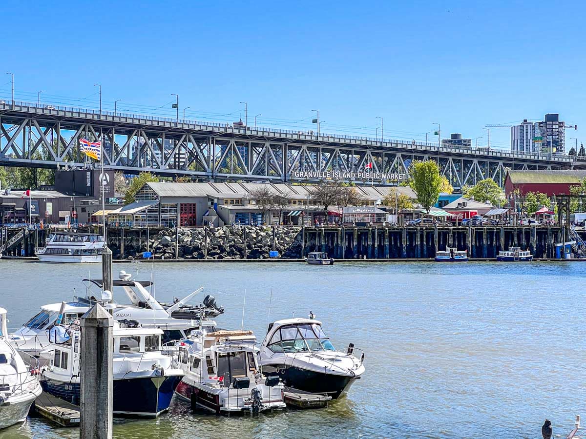 large public market on granville island with road bridge over top and boats in harbour in foreground.