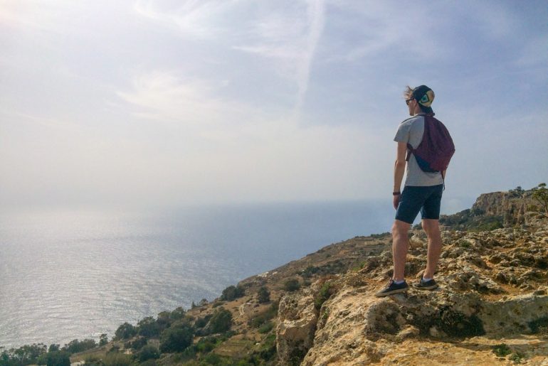 man standing on cliff edge with ocean below malta sightseeing