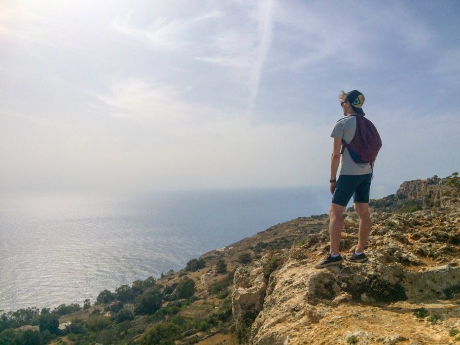 man standing on cliff edge with ocean below malta sightseeing