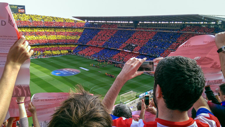 people in large stadium holding up coloured paper with open sky above.