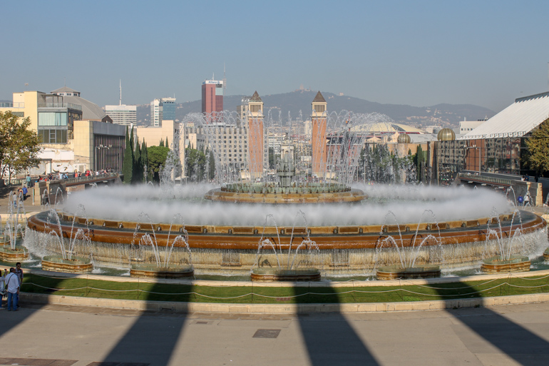 circular fountain spraying water with city buildings behind.