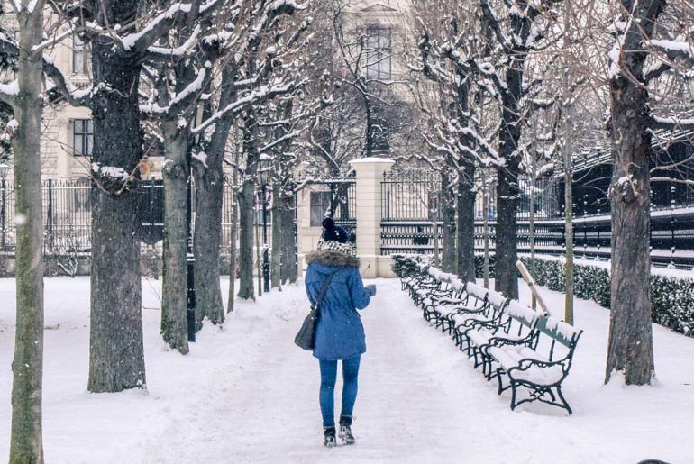 Frau in blauem Mantel läuft durch schneebedeckten Park Wien