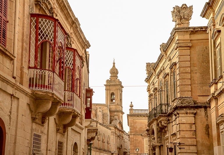 Sandsteinfarbene Gebäude entlang steinerner mit altem Turm und roten Fenstern in Mdina Malta