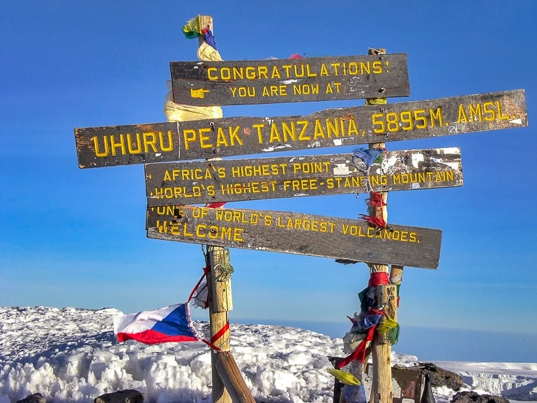 Holzschild und bunte Flaggen auf Spitze von Kilimandscharo