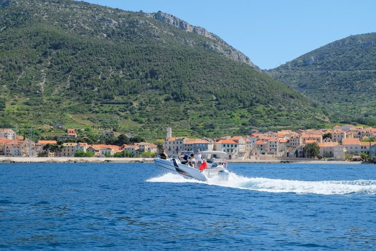 Speedboot im blauen Wasser mit kroatischem Dorf im Hintergrund