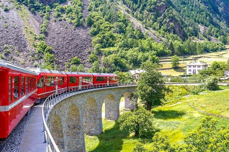 Roter Zug auf kurviger Brücke mit grünen Bergen im Hintergrund Schweiz