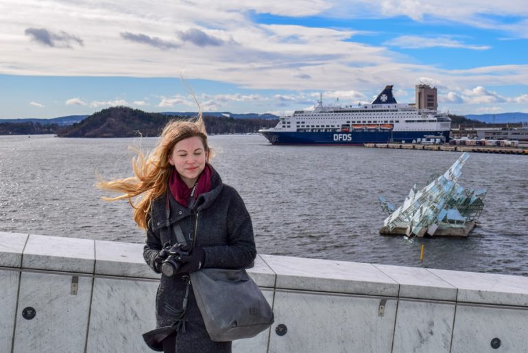 Frau mit vom Winde verwehtem Haar mit Hafen und Schiff im Hintergrund Oslo