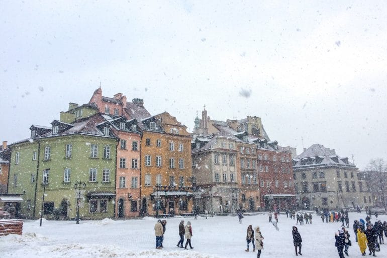 colourful buildings through snow flakes with people must see places in europe in winter warsaw