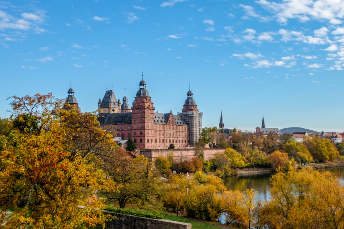 Rotes Schloss neben Bäumen in Herbstfarben und Fluss Aschaffenburg Bayern