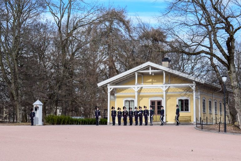 Kleines gelbes Gebäude mit Wachen im Vordergrund und Bäumen dahinter Oslo