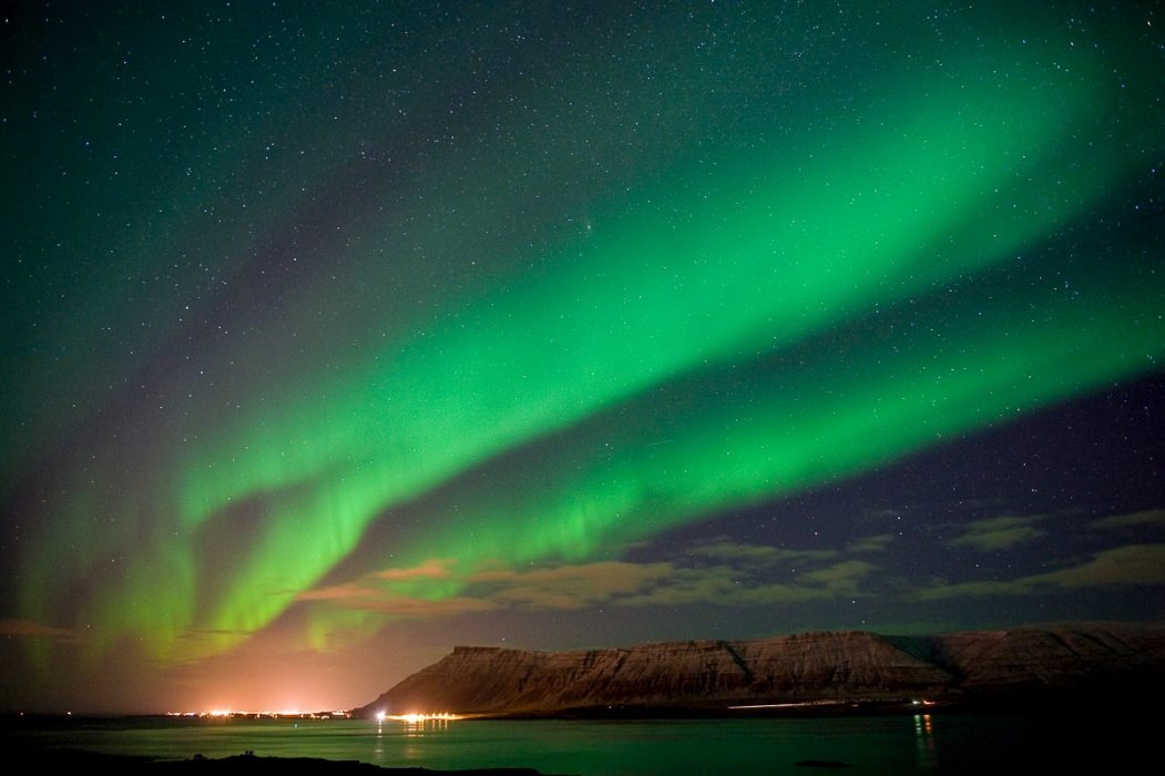 green lights over lit up city and mountain trips to see the northern lights iceland