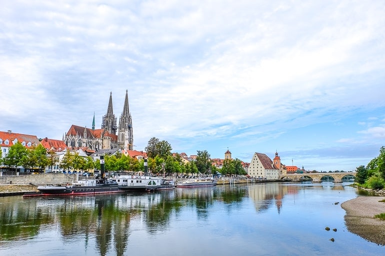 river with boats and bridge over it with cathedral behind in regensburg germany
