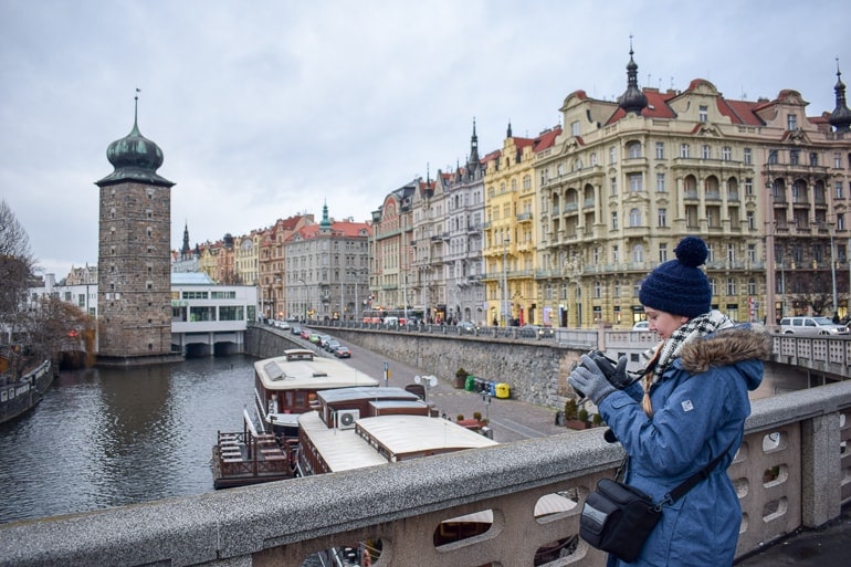 girl in winter hat taking photo of old town buildings european hostels prague czech republic