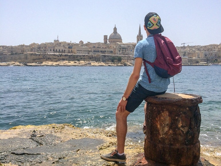 Mann mit Mütze und Rucksack schaut auf das Wasser zum Hafen Malta