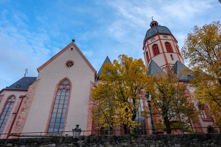 Bunte Fasade von Kirche mit Glasfenster und grünen Bäumen Mainz