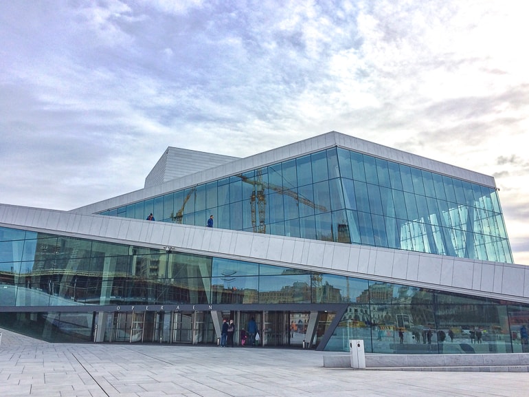 large glass opera house with entrance doors and cloudy sky above in oslo.