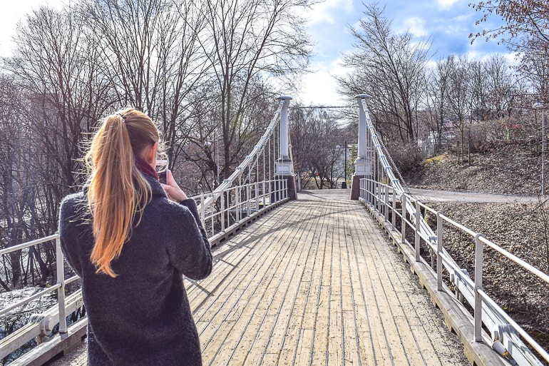 girl in coat from behind taking photo of wooden bridge.