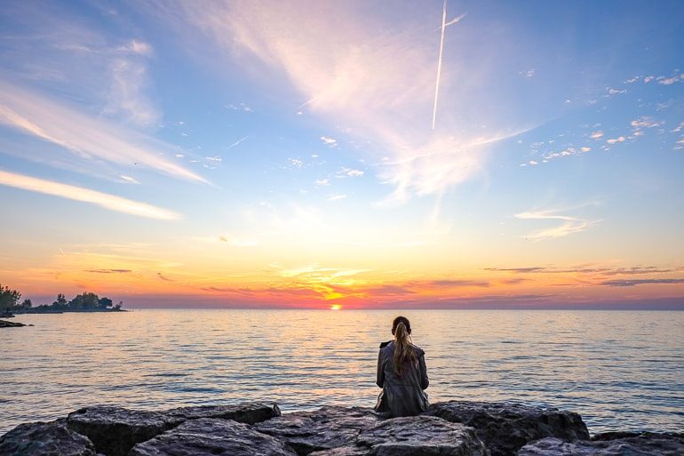 Frau sitzt auf Felsen mit Sonnenaufgang und See im Hintergrund Toronto Kanada