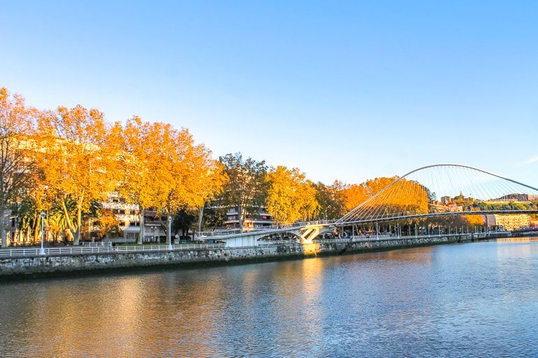 Weiße Brücke mit Kurven über Fluss und herbstlichen Bäumen Bilbao Spanien