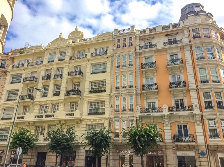 beautiful spanish building with black balconies and green palm trees below in front.