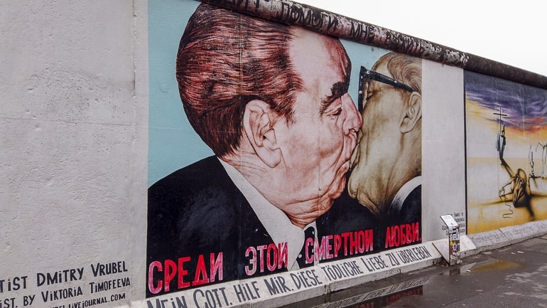 Zwei Männer küssen sich auf Bild an Berliner Mauer.