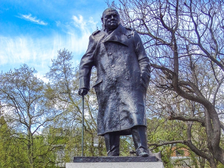 statue of man churchill with cane and trees behind.