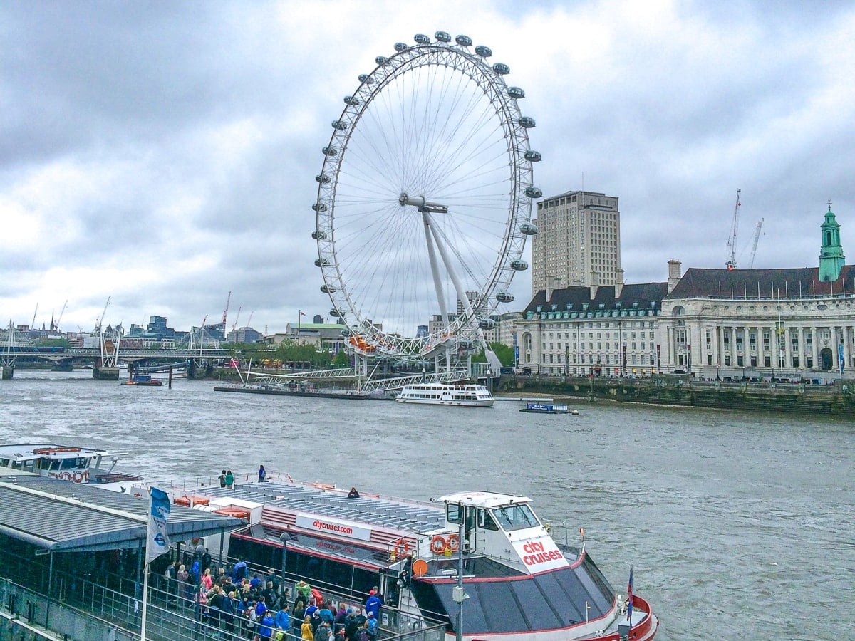 tour boat on river loading with people with london eye ferris wheel behind.