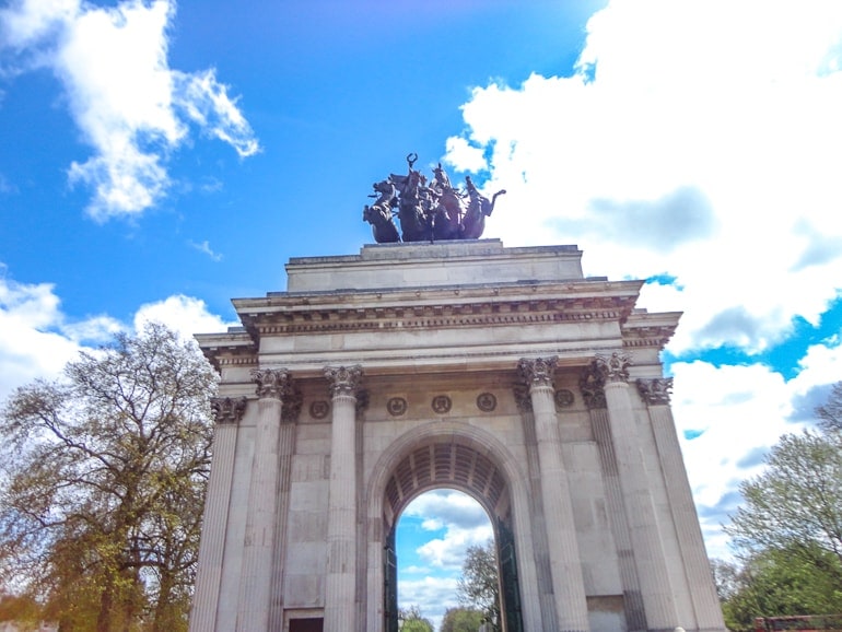 stone archway with statue on top and blue sky above in hyde park in london.