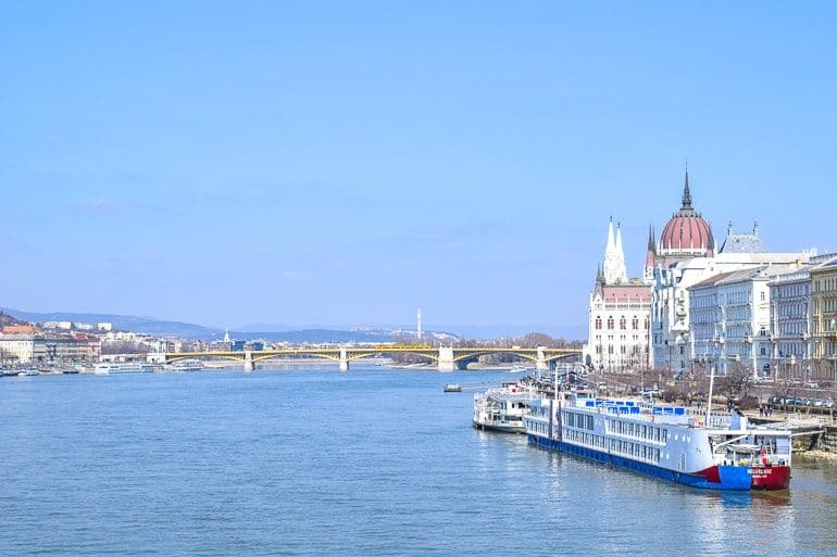 Blauer Fluss Donau mit langem Boot und großen Gebäuden im Hintergrund Budapest