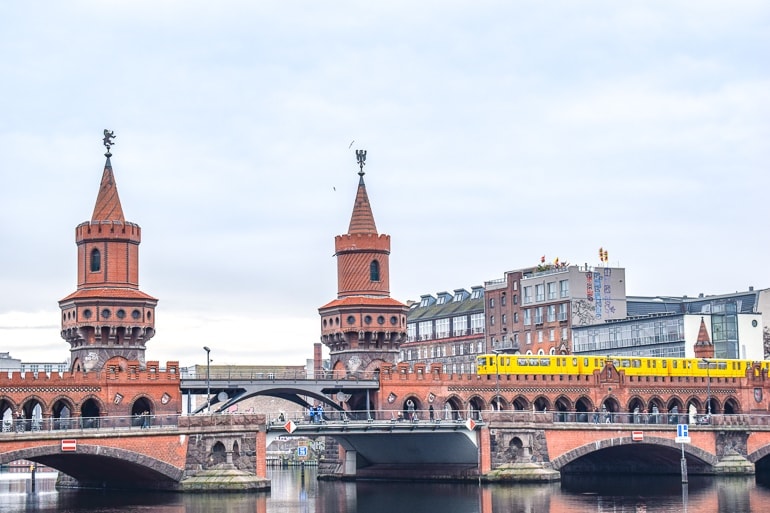 red bridge with two towers over river and yellow train on it berlin