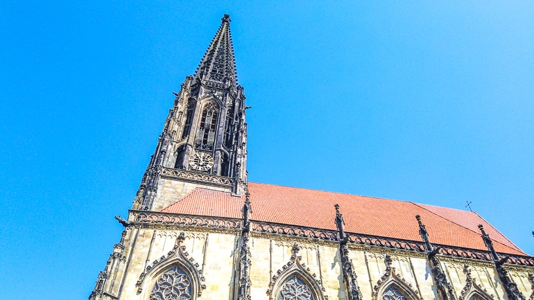 Schwarzer Kirchturm verbunden mit rotem Dach und blauem Himmel Münster