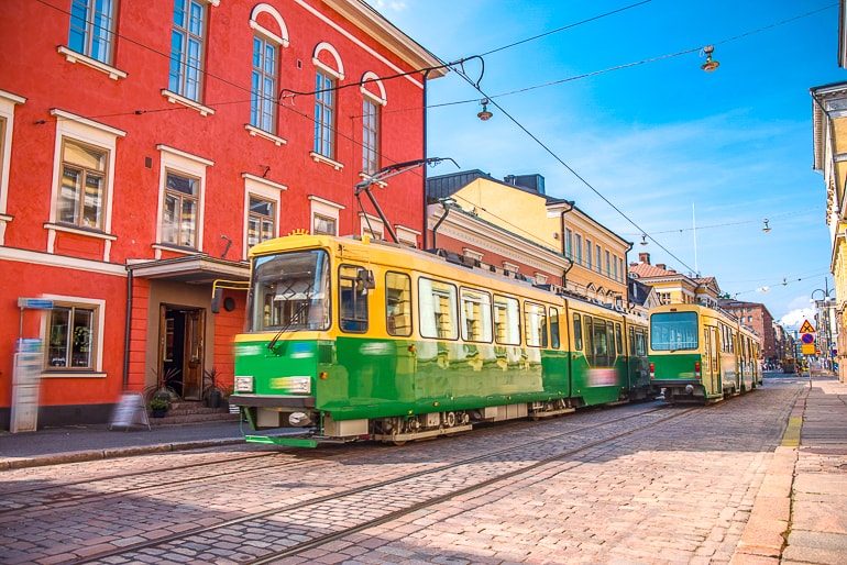Grüne Straßenbahn fährt an rotem Gebäude vorbei in Helsinki Finnland