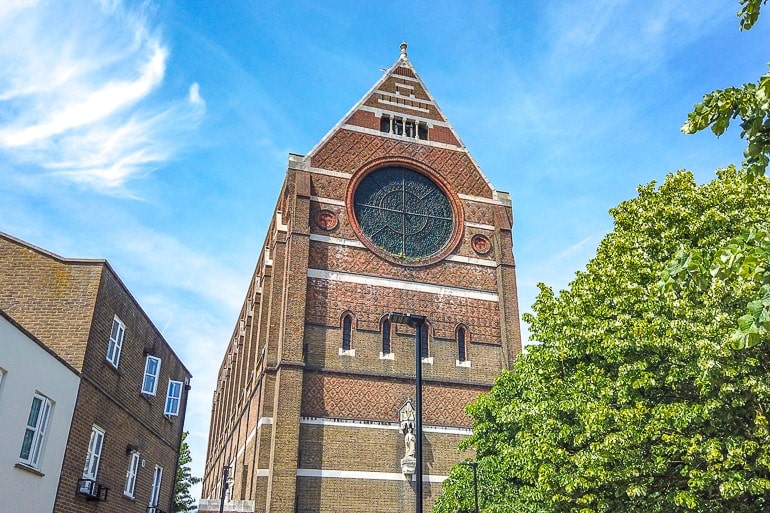 brown brick church with stain glass window and blue sky behind.