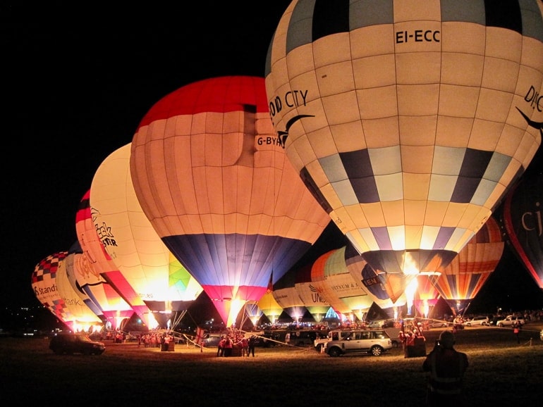 hot air balloons getting inflated in a row at night.
