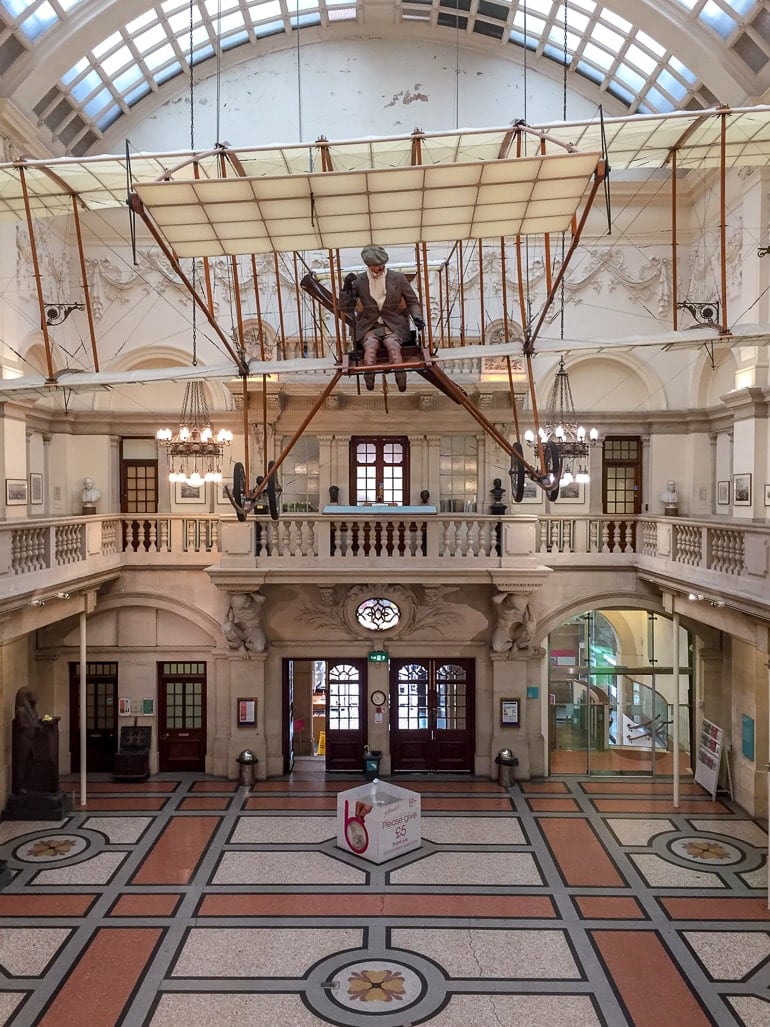 man in model airplane hanging from museum ceiling in bristol.