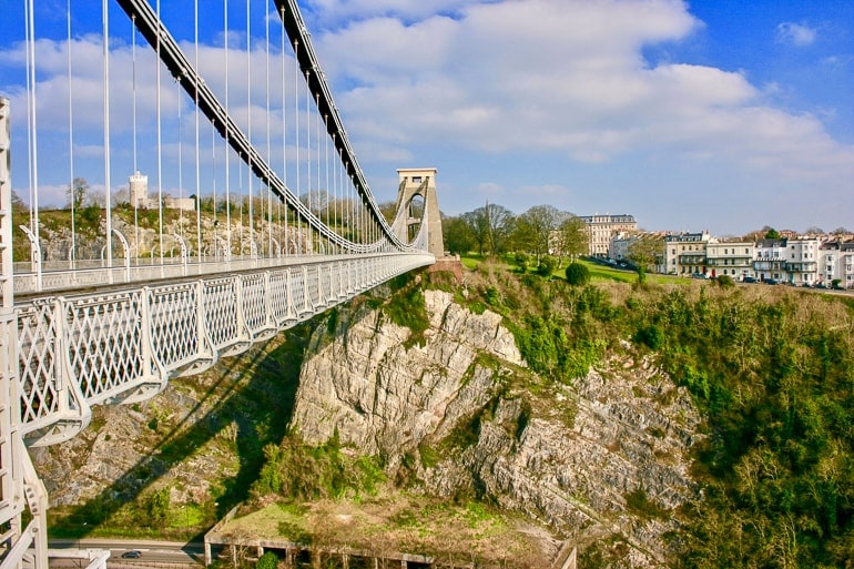 suspension bridge crossing large rocky gorge with city houses beside.