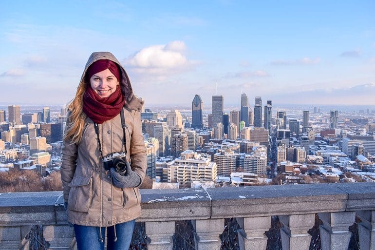 girl with tan jacket and red scarf holding camera with city behind things to do in montreal