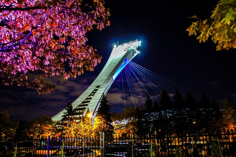 white arena tower with lights seen through trees in montreal olympic park.