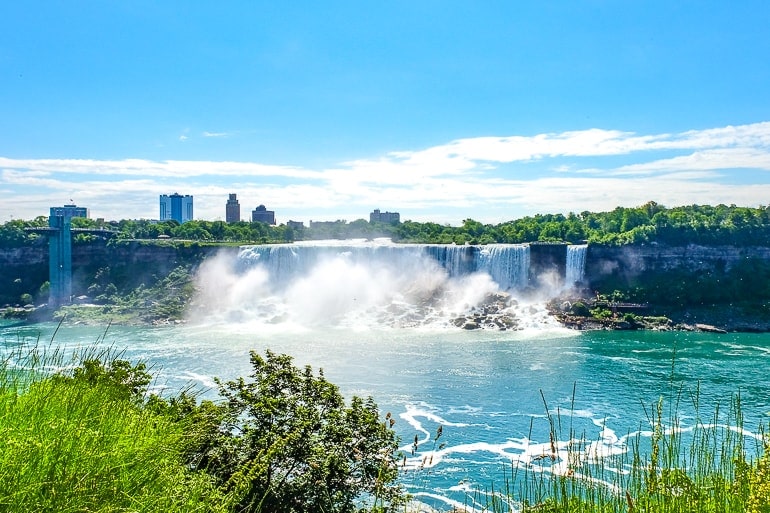 waterfalls from a distance with green shrubs in front american falls niagara falls