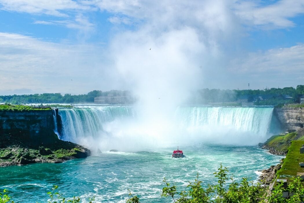 Blaues Wasser und Wasserfälle mit kleinem Boot im Fluss darunter Niagara Falls Kanada