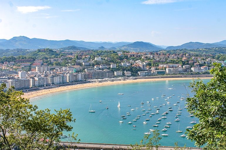 blue bay with boats and sandy beach around it with buildings beautiful cities in spain san sebastian