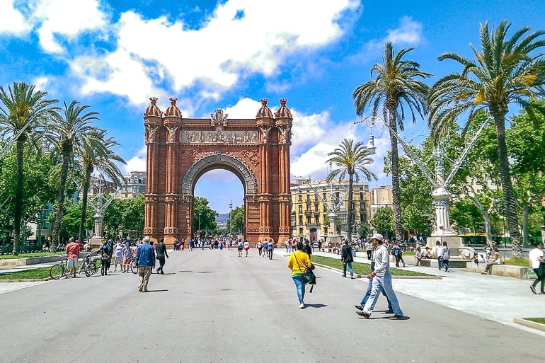 red archway with sidewalk and palm trees around and people barcelona beautiful cities to visit spain