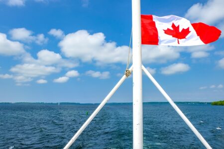 canada flag waving in wind at back of ship with blue lake below canada sightseeing