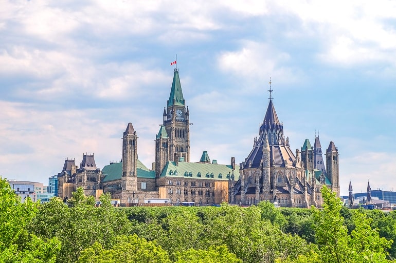 Parlamentsgebäude aus Stein mit Türmen und grünen Bäumen im Vordergrund in Ottawa Kanada.
