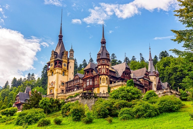 brown and yellow castle with towers and green bushes peles castle day trip from brasov