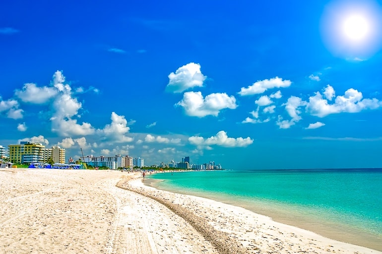 white sandy beach with blue ocean and buildings behind miami sightseeing south beach