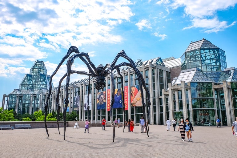 large metal spider in front of glass building one day in ottawa