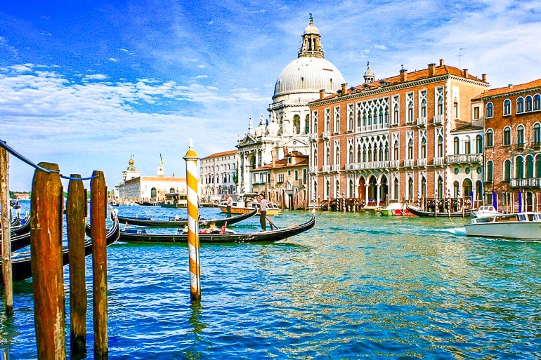white dome building with brown building beside on canal bank with boats in grand canal one day in venice italy