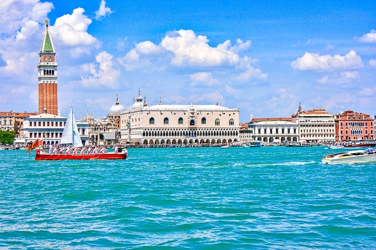 Blaues Wasser mit rotem Boot und Turm im Hintergrund ein Tag in Venedig